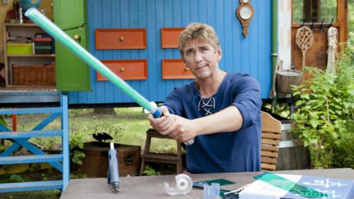 Fritz steht vor dem Bauwagen und hält ein grünes Laserschwert in der Hand.