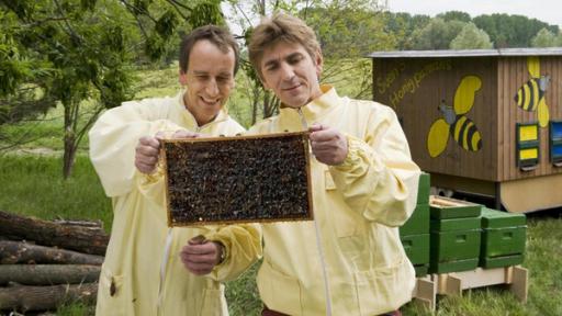 Fritz Fuchs steht vor einem Bienenwagen. Er trägt eine gelbe Regenjacke und seine rote Hose. 