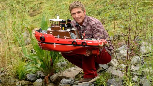 Fritz hockt am Flussufer mit dem Boot Heinz 1 in der Hand.