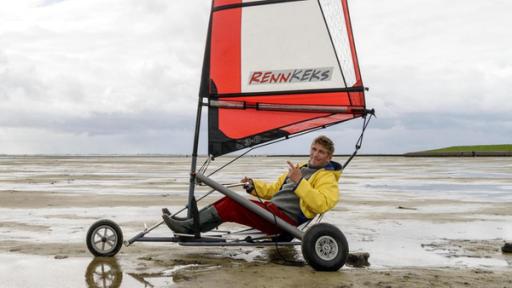 Fritz Fuchs sitzt in einem Strandsegler. Es ist Ebbe, das Meer hat sich zurückgezogen.