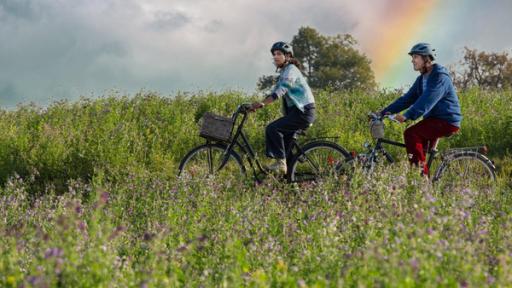 Löwenzahn - Regenbogen Teaser MT25 | Rechte: ZDF Fritz und Yasemin fahren mit dem Fahrrad durch Wiesen - im Hintergrund ist ein Regenbogen am Himmel zu sehen