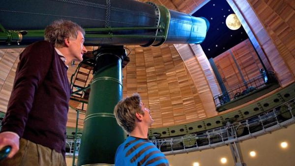 Fritz Fuchs steht mit einem Mitarbeiter des Observatoriums neben einem riesigen Teleskop und betrachtet den Mond. | Rechte: ZDF