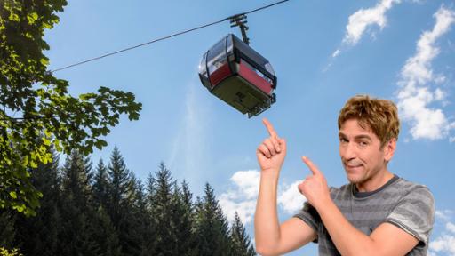 Fritz zeigt mit dem Finger auf eine Seilbahn, die über ihm schwebt