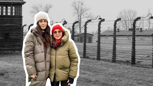 Die Auschwitz-Überlebende Eva Umlauf und Reporterin Teresa Betz stehen in Auschwitz vor einem Stacheldrahtzaun. Beide Frauen sind winterlich gekleidet und blicken ernst. Im Hintergrund Wachtürme, Stacheldrahtzäune und kahle Bäume in Schwarz-Weiß-Farben.