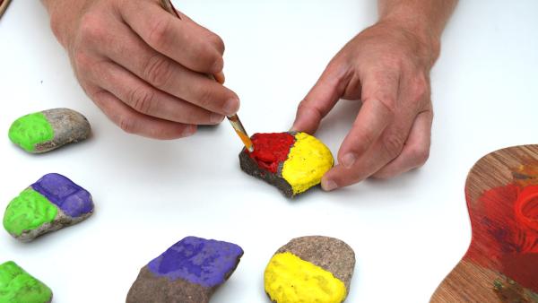 Bevor du mit dem Bemalen beginnst, achte darauf, jede Farbe ungefähr gleich oft zu verwenden. Bemale immer nur eine Hälfte des Steins mit einer Farbe.  | Rechte: KiKA