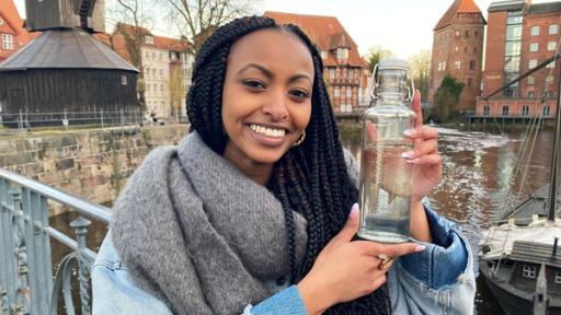 Reporterin Luam hält eine Glasflasche Wasser in der Hand.