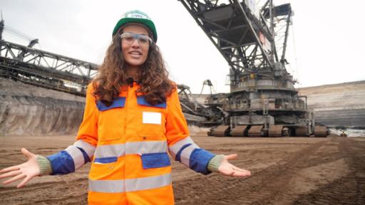 Mona steht vor einem riesengroßen Schaufelradbagger im Tagebau Garzweiler.