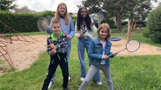 Inna, Petro und Uliana stehen auf einem Spielplatz. Sie halten Federballschläger in der Hand.