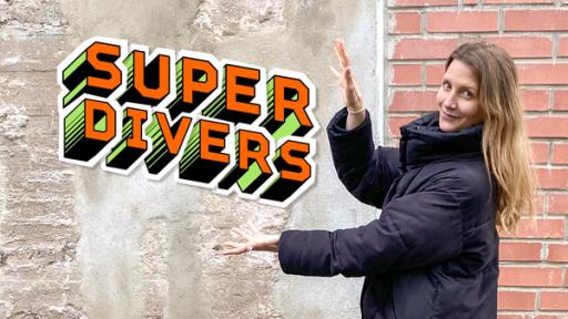 Reporterin Jana vor einer Mauer, sie zeigt auf die Aufschrift "SUPERDIVERS".