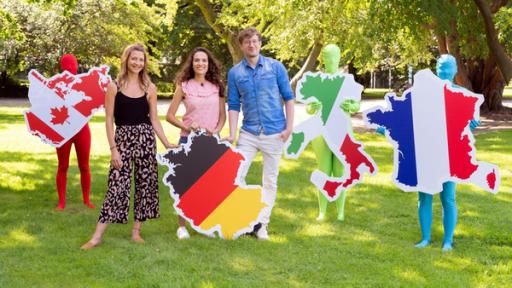 Jana, Mona und Robert halten auf einer Wiese Umrisse Deutschlands, Kanadas, Italiens und Frankreichs hoch.
