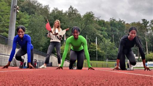 Die Drillinge Dörte, Dorina und Dorinda in Startposition auf dem Sportplatz. Hinter ihnen schlägt Jana die Start-Klappe.