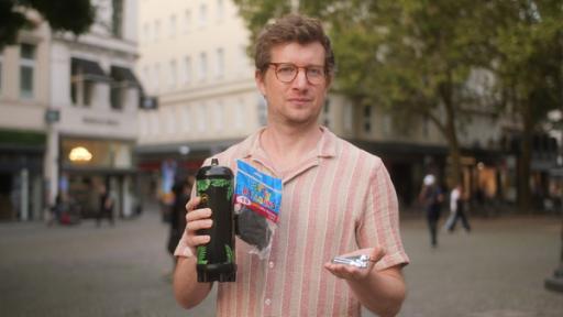 Reporter Robert Meyer hält kleine Sahnekartuschen, schwarze Luftballons und eine große Lachgas-Kartusche in der Hand.