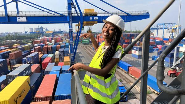 Reporterin Luam steht auf einem Brückenkran im Duisburger Hafen. Im Hintergrund sieht man hunderte Überseecontainer. | Rechte: WDR/tvision