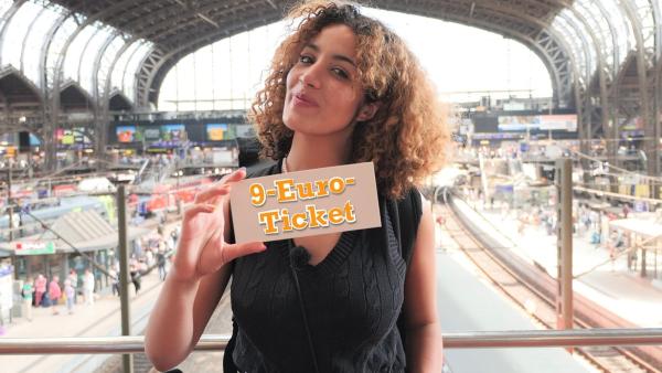 Tessniem steht am Bahnhof und hält ein Ticket in die Kamera, auf dem der Schriftzug '9-Euro-Ticket' steht. | Rechte: WDR | tvision