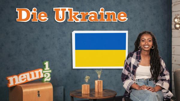 Luam sitzt auf einem Stuhl neben einem kleinen Tisch und dem neuneinhalb-Logo. Auf einer blauen Wand steht der Schriftzug "Die Ukraine" und hinter Luam ist die ukrainische Flagge zu sehen. | Rechte: WDR/tvision