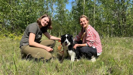 Biologin Annegret Grimm-Seyfarth und Moderatorin Jana hocken im Gras. Zwischen ihnen sitzt der Border Collie Zammy.