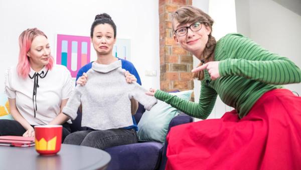 Die drei Wissenschaftlerinnen sitzen gemeinsam auf einem Sofa, Linh (mi.) hält einen eingelaufenen, kleinen Pullover in ihren Händen und schaut traurig, Patrizia (re.) zeigt erstaunt darauf. | Rechte: ZDF/Martin Vogel