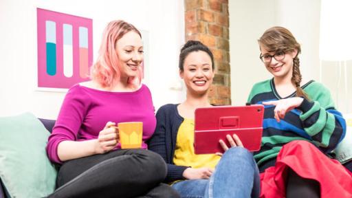 Die drei Wissenschaftlerinnen Johanna, Linh und Patrizia sitzen in ihrem Co-Working-Space auf einem Sofa und schauen gemeinsam in ein Tablet mit pinker Hülle.