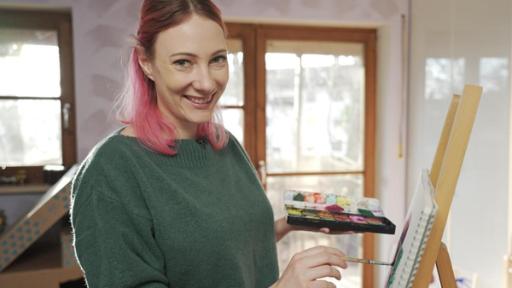 Princess Johanna (li.) mal mit Farbe auf eine Leinwand, die auf einer Staffelei (re.) steht. In einer Hand hält sie einen Tuschkasten mit Wasserfarben.