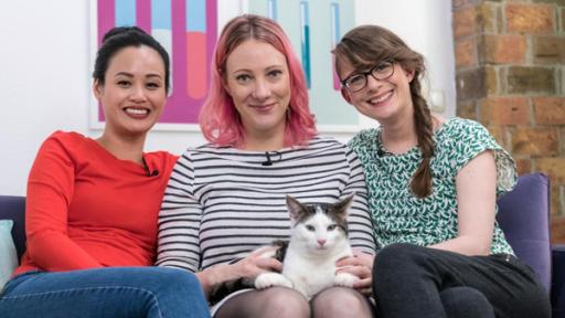 Die drei Princesses sitzen gemeinsam auf dem Sofa, Johanna (mi.) hat Studiokater Emil auf dem Schoß.