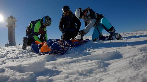 Um Snowkiten zu können, muss man erst einmal den Kite, also den Lenkdrachen beherrschen. Vorher werden auch keine Skier angeschnallt. Das lernen Laura (r.) und Emilio (l.) bei Trainer Matthias (M.). | Rechte: ZDF/Sandra Palm