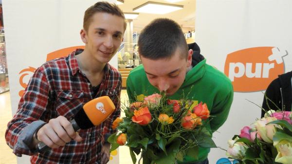 Eric Mayer, pur+ Stuntman des Wissens beim Geruchstest. Passanten sollen am Geruch feststellen, welchen Blumenstrauß, die vorher mit einem Duft eingesprüht wurden, sie eher kaufen würden. | Rechte: ZDF/Sandra Palm