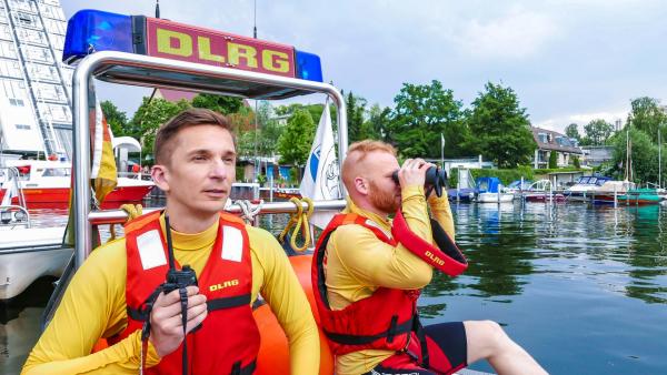 Eric sitzt zusammen mit einem Rettungschwimmer der DLRG in einem Boot der DLRG. Der Rettungsschwimmer schaut durchs Fernglas. Eric hät ein Fernglas in der Hand. Beide blicken auf den See hinaus. | Rechte: ZDF
