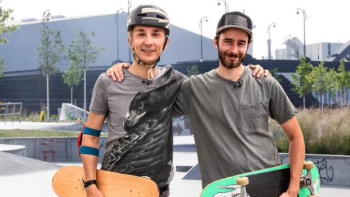 Eric Mayer und sein Trainer stehen auf einer Skateranlage. Sie halten ihre Boards im Arm. Eric trägt einen Schutzhelm und Ellbogenschützer. Der Trainer trägt eine Kappe. Beide schauen lächelnd nach vorne.