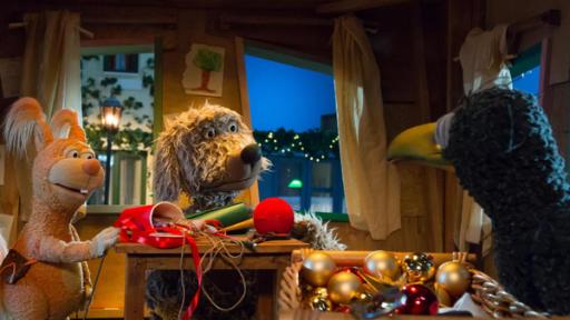 Ella, Buffo und Rudi sind im Baumhaus und schauen sich an. Zwischen ihnen auf dem Tisch liegen Bastelutensilien, im Vordergrund Weihnachtsbaumkugeln.