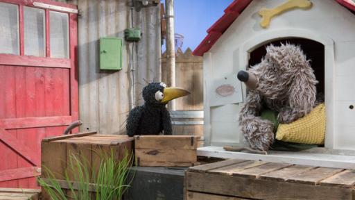 Rabe Rudi und Hund Buffo schauen sich vor Buffos Hundehütte an.