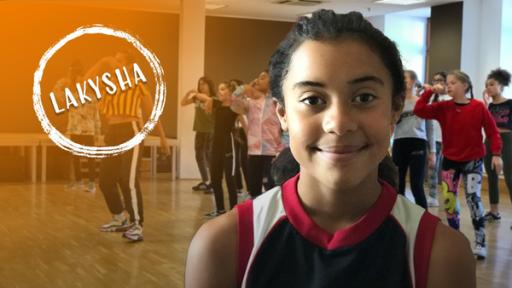 Vorne steht Lakysha im Sportdress in einem Tanzsaal und lächelt. Im Hintergrund eine Gruppe beim Tanzen. Links der Name Lakysha kreisförmig weiß umrandet.