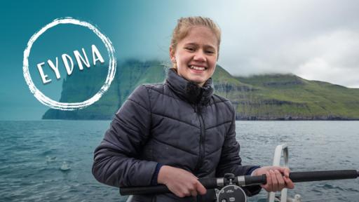 Das Mädchen Eydna sitzt mit einer Angel auf einem Boot im Meer und lächelt.