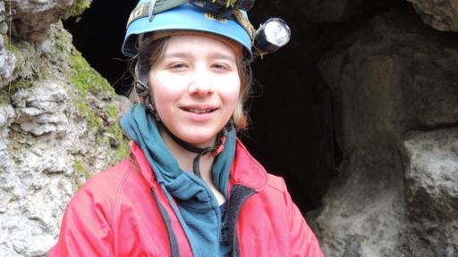 Mädchen mit Helm vor einem Höhleneingang