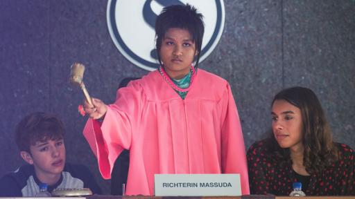Eine Person mit rosaner Robe und einem Gerichtshammer.