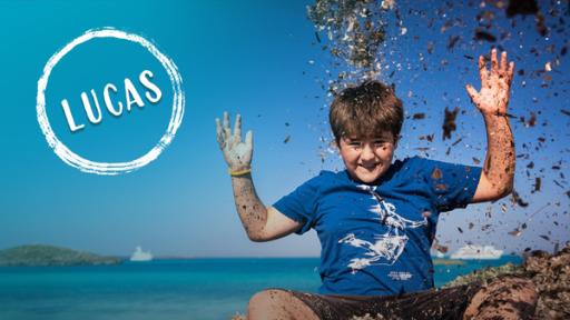 Lucas wirft lachend am Strand Seegras in die Luft.