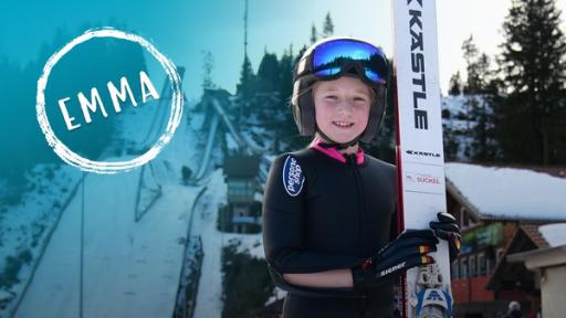 Eine Skispringerin mit Helm, Anzug und ihren Ski vor einer schneebedeckten Schanze