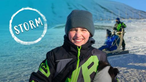 Storms Welt schmilzt - die Arktis und das Klima | Rechte: hr Storm trägt eine Mütze und einen Schneeanzug. Er hat einen kleine Husky-Welpen im Arm und grinst in die Kamera. Im Hintergrund ist eine karge Schneelandschaft, durch die ein Hundeschlitten-Gespann fährt.