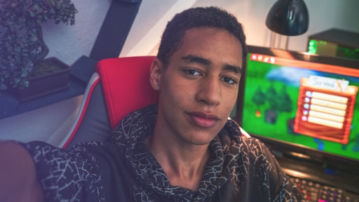 Jonathan (Rolle Malik) macht ein Selfie von sich. Im Hintergrund steht ein PC.