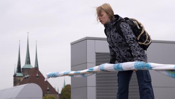 Martha (Luna Kuse) hat vor, ein großes Plakat von einem Dach hängen zu lassen. | Rechte: MDR/Saxonia Media/Katharina Simmet