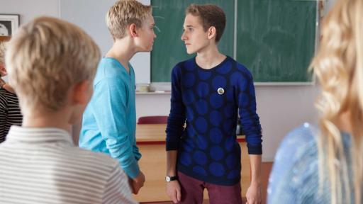 Zwei Jungen in einem Klassenraum schauen sich kampfeslustig an.