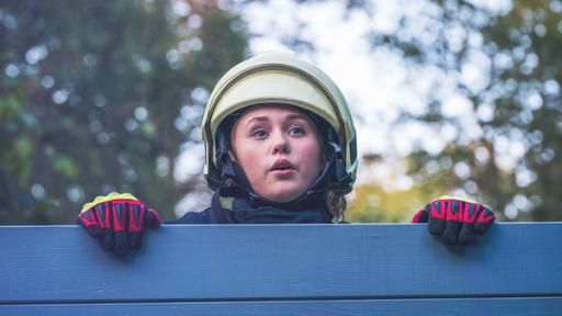 Jugendliche mit Helm und Handschuhen schaut über eine Bretterwand