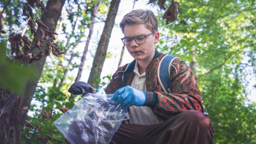Jugendlicher mit Plastiktüte in der Hand im Wald