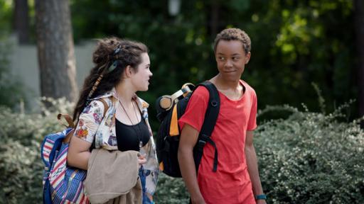 Ein Junge und ein Mädchen mit Schulrucksack auf dem Rücken gehen durch einen Park.