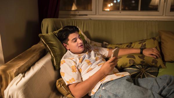 Orkan liegt auf dem Sofa und schaut auf sein Smartphone | Rechte: MDR/Saxonia Media/Felix Abraham