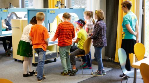 Kinder stehen an einem beleuchteten Tisch mit Kamera