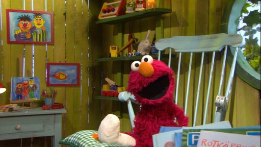 Das rote Fellmonster Elmo sitzt mit einem Gipsbein auf einem grünen Stuhl in seinem Spielehaus.