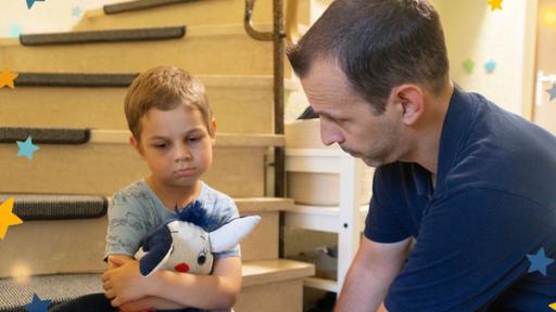 Leon hält seine Kuscheltier Fidi im Arm und sitzt traurig auf der Treppe. Vor ihm sitzt sein Papa.