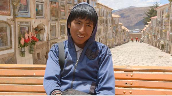 Portrait von Juan-Carlos. Er sitzt auf einer Holzbank und trägt eine blaue Kapuzen-Jacke. Er lacht in die Kamera. | Rechte: ZDF