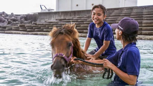  Uruné reitet auf dem Pony im Wasser, der Trainer hält die Zügel des Ponys in der Hand. Uruné lacht glücklich den Trainer an. | Rechte: ZDF