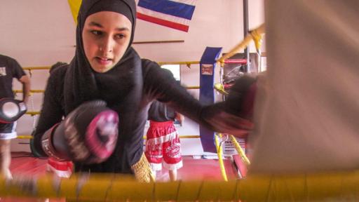 Nouhaila ist beim Training im Boxring. Sie trägt Boxhandschuhe und boxt gegen einen Boxsack.